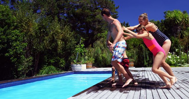 A young Caucasian woman playfully pushes a man into a swimming pool, both enjoying a sunny day outdoors. Their spontaneous action captures the essence of summer fun and leisure.