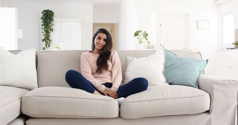 Relaxed woman sitting cross-legged on beige sofa in cozy home interior