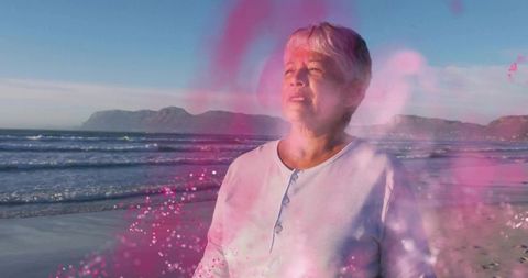 Serene Senior Woman Enveloped by Pink Powder on Beach at Sunrise