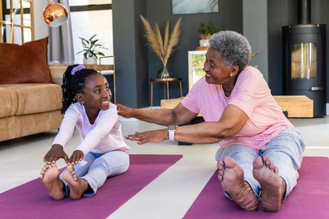 African american grandmother and granddaughter stretching on yoga mats in sunny living room