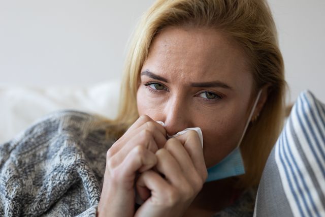 A caucasian woman sitting on the couch at home with a sad expression on her face. she is pressing a napkin on her nose.
