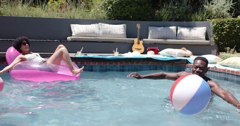 Summer backyard pool party friends lounging on inflatable float playing with beach ball