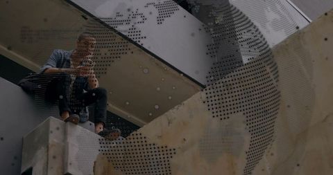 Solitary man on concrete ledge using smartphone beneath perforated metal panel in urban garage