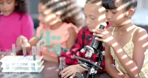 Girl peering into microscope during hands-on elementary science experiment with classmates