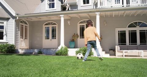 African american boy walking toward soccer ball on suburban front lawn by porch of classic home