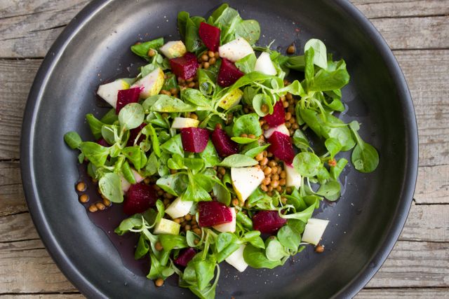 This colorful salad features fresh beets, lentils, and mixed greens, arranged on a rustic wooden table. Perfect for use in health food blogs, vegetarian recipe articles, or as appetizing visual content for restaurants and catering services promoting fresh, nutritious, and organic meals.