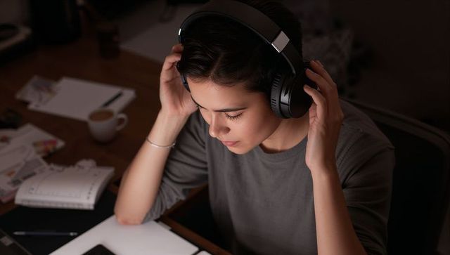 Focused asian woman wearing headphones concentrating on laptop while working late at desk