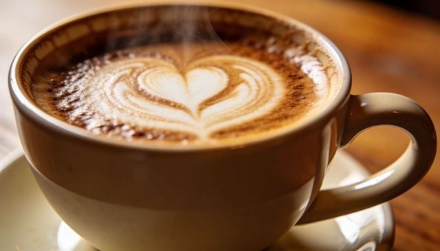 Steaming heart latte in beige ceramic cup on warm wooden table with cozy foam art