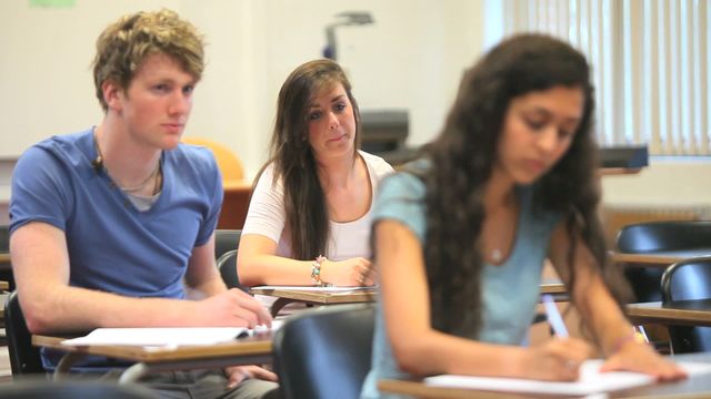 Group of college students attentively participating in a class session. Ideal for educational content, tutoring services, academic achievement promotions, study group resources, and school related brochures.