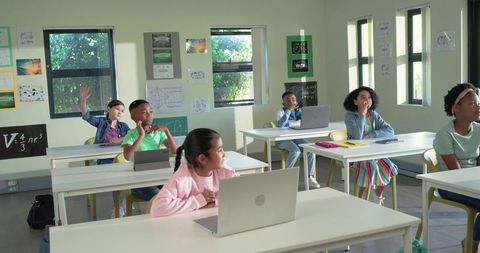 Diverse elementary students using laptops in bright classroom during interactive learning