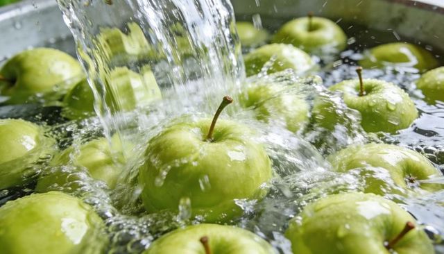Washing green apples under flowing water, fresh droplets and splashing ripples close-up