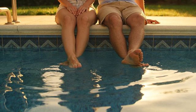 Couple sitting at pool edge dipping feet in water during golden hour summer relaxation