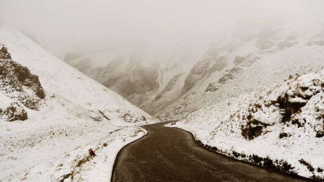 Snow-covered winding road through mountainous terrain on a misty winter day, providing a serene and peaceful scenery perfect for backgrounds, travel blogs, winter adventure promotions, or holiday-themed content.