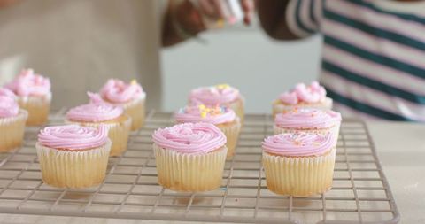 Senior and young women baking vanilla cupcakes with pink frosting together in home kitchen