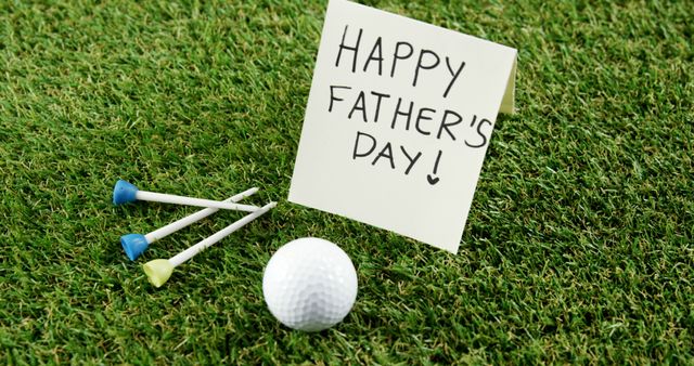 A greeting card with Happy Father's Day! is placed on a golf course next to a golf ball and tees, with copy space. It suggests a celebration of Father's Day for those who enjoy the sport of golf.