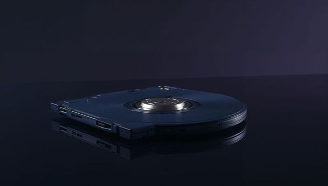 Resting dark-blue disc cartridge mirroring on glossy surface with metallic hub and side ports
