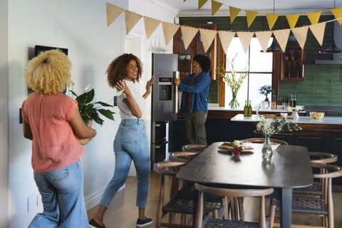 Friends decorating kitchen with bunting and plants for cozy home gathering
