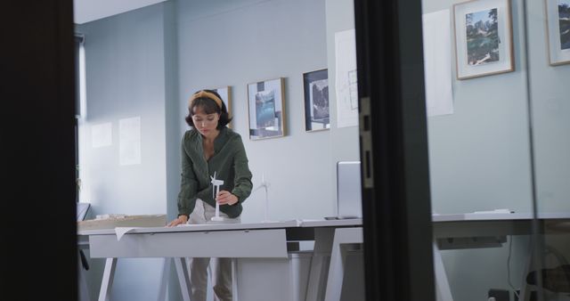 This photo depicts a female architect using a scanner to process architectural documents in her modern office. The setting includes sleek furniture, artwork on the walls, and a professional atmosphere. This image can be used for projects related to architecture, interior design, professional women, modern workplaces, or technology in creative fields.