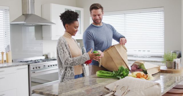 Image of happy diverse couple unpacking groceries in kitchen. Love, relationship and spending quality time together at home.