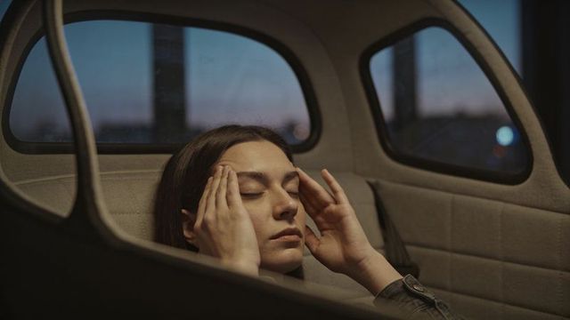 Woman pressing temples in compact car rear seat at dusk conveying fatigue and introspection