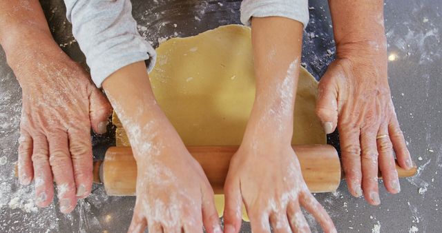 Grandparent and child baking together, using a rolling pin to flatten dough on a floured surface. Perfect for articles about family activities, cooking tutorials, or promoting family bonds through shared activities.