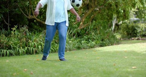 Man juggling soccer ball on sunny backyard lawn wearing white shirt and blue jeans