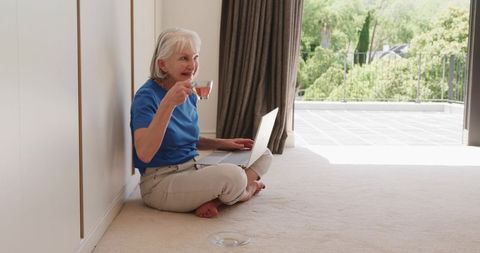 Senior Woman Relaxing with Laptop by Balcony Door