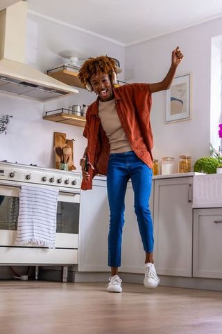 African american woman dancing in bright kitchen wearing headphones and holding phone