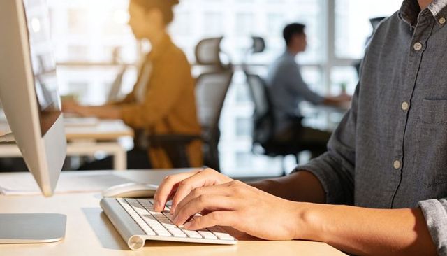 Hands Typing on White Keyboard in Modern Open Office Emphasizing Productivity and Focus