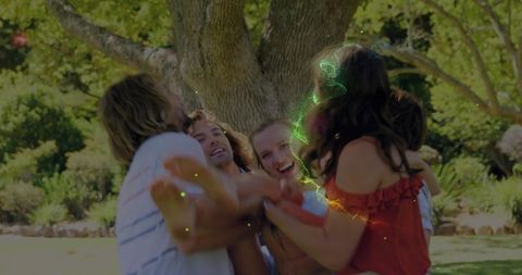 Sunlit friends embracing under oak tree with neon sparkles, outdoor summer celebration