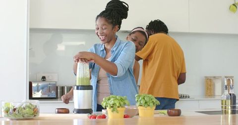African american family preparing green smoothie, cooking together in bright modern kitchen