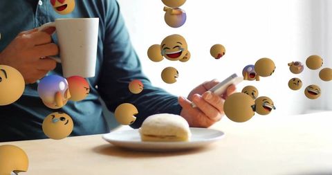 Man enjoying coffee, scrolling smartphone as emojis playfully float around kitchen table