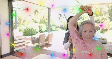 Asian senior woman exercising with caregiver assistance on home deck using dumbbell
