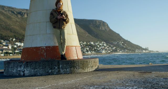 Young Man Using Smartphone Leaning Against Coastal Lighthouse - Download Free Stock Images Pikwizard.com