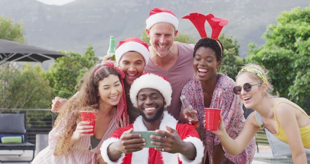 Group of diverse friends celebrating Christmas outdoors, smiling joyfully while taking group selfie. Perfect for holiday cards, social media posts, blog articles about holiday celebrations, and promotional materials for festive events.