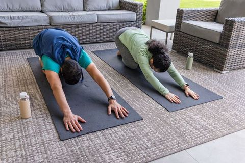 Couple practicing yoga childs pose on covered patio with wicker seating and cushions
