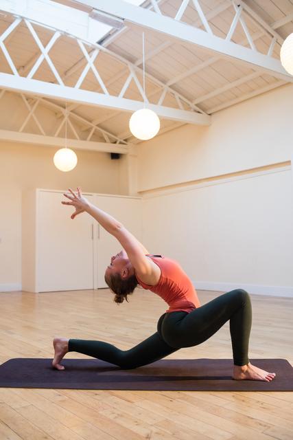 Woman practicing yoga on exercise mat in modern fitness studio with wooden floor and white walls. Ideal for promoting yoga classes, fitness programs, wellness retreats, and healthy lifestyle content.