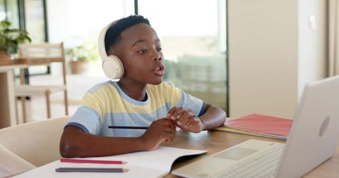 African american boy wearing headphones studying on laptop for remote learning at home