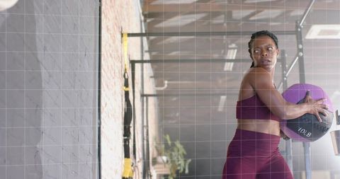 Woman holding purple 10 lb medicine ball twisting core workout near trx straps studio