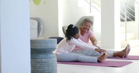 African american grandmother and granddaughter stretching together on home yoga mats
