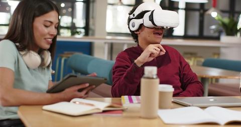 Diverse students testing VR headset and studying together in modern campus commons