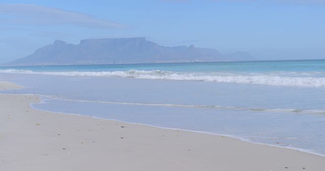 A serene beach scene showcases gentle waves and a mountain backdrop - Download Free Stock Photos Pikwizard.com