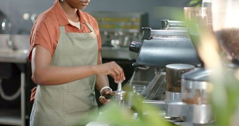 African american barista tamping espresso grounds at modern cafe counter with green apron
