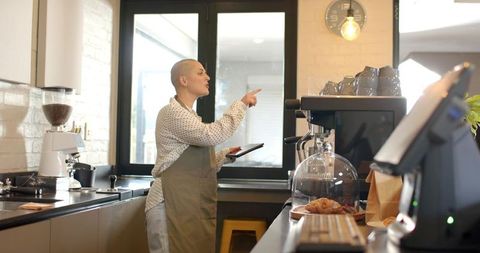 Barista pointing while holding tablet behind modern espresso counter with pastry display