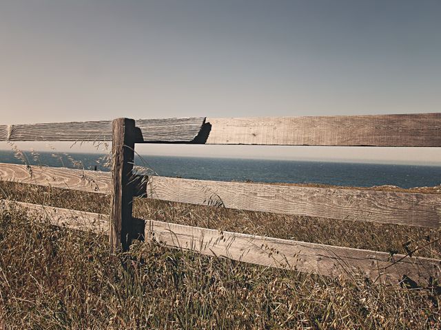 Wooden fence standing on grassy terrain providing a tranquil seaside view. Ideal for illustrating themes of nature, relaxation, coastal living, and quiet country settings. Useful for blog posts, travel guides, calendars, or wall decor representing serenity and simplicity.