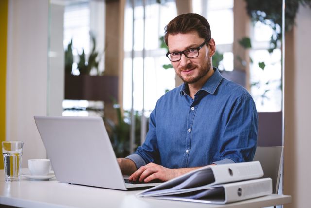 Portrait of confident young businessman working on laptop at creative office