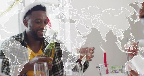 Pouring sparkling wine wearing santa hat at festive dinner with world map overlay