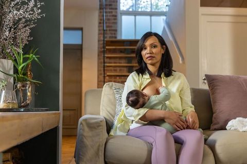 Mother breastfeeding baby on sofa in cozy living room with natural light and plants
