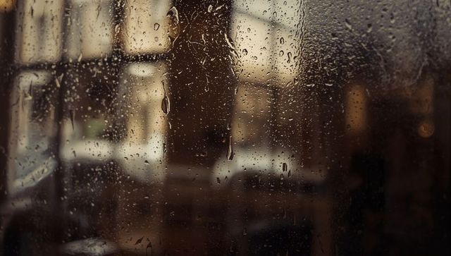 Rain-soaked window dripping droplets over blurred warm cafe interior moody bokeh ambience
