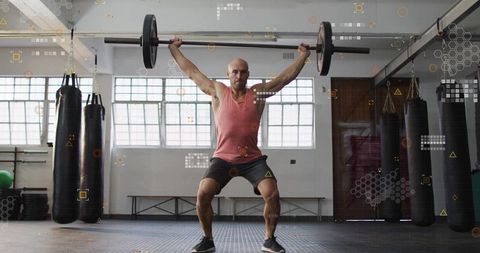 Man Performing Overhead Squat While Lifting Barbell in Industrial Gym with Punching Bags